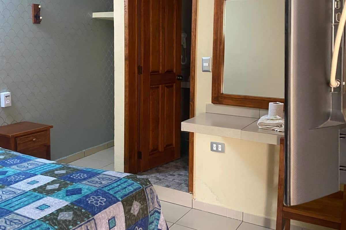 A bedroom with a bed, a wooden door, a mirror, and a small bedside table.