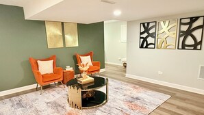 A modern living room with two orange armchairs, a black coffee table, and abstract wall art. - Haven Suite- Modern 1BR Near Gurnee Mills, Six Flags, Naval Base, Area Hospitals (Gurnee)