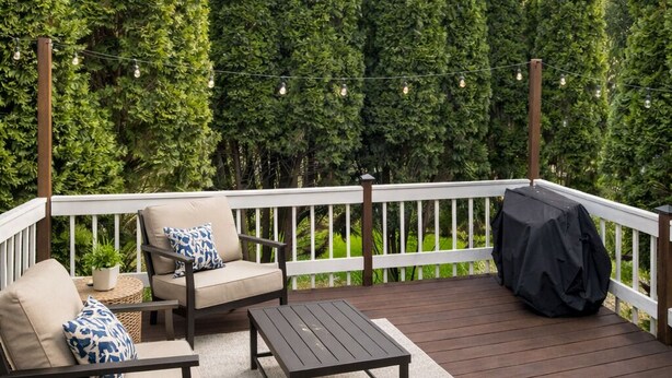 A wooden deck with a white railing, two beige sofas with patterned cushions, a small round table, and a barbecue grill. - Haven Suite- Modern 1BR Near Gurnee Mills, Six Flags, Naval Base, Area Hospitals (Gurnee)