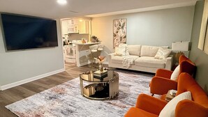 A living room with a sofa, a coffee table, and a TV. There is a kitchen area with cabinets and a microwave. - Haven Suite- Modern 1BR Near Gurnee Mills, Six Flags, Naval Base, Area Hospitals (Gurnee)