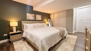 A bedroom with a large bed, two bedside tables with lamps, a dresser, a mirror, and a wardrobe. - Haven Suite- Modern 1BR Near Gurnee Mills, Six Flags, Naval Base, Area Hospitals (Gurnee)