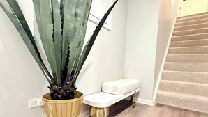 A staircase with a white cushioned bench and a large potted plant with spiky leaves. - Haven Suite- Modern 1BR Near Gurnee Mills, Six Flags, Naval Base, Area Hospitals (Gurnee)