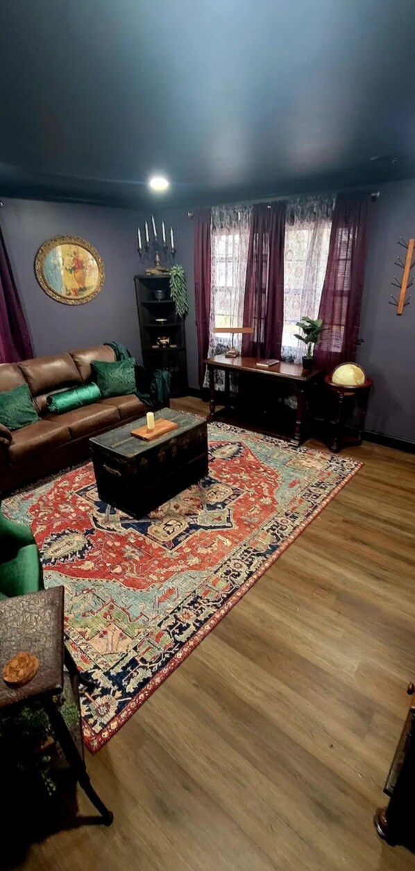 Un salón con un sofá de cuero marrón, una mesa de centro de madera oscura y una alfombra estampada.