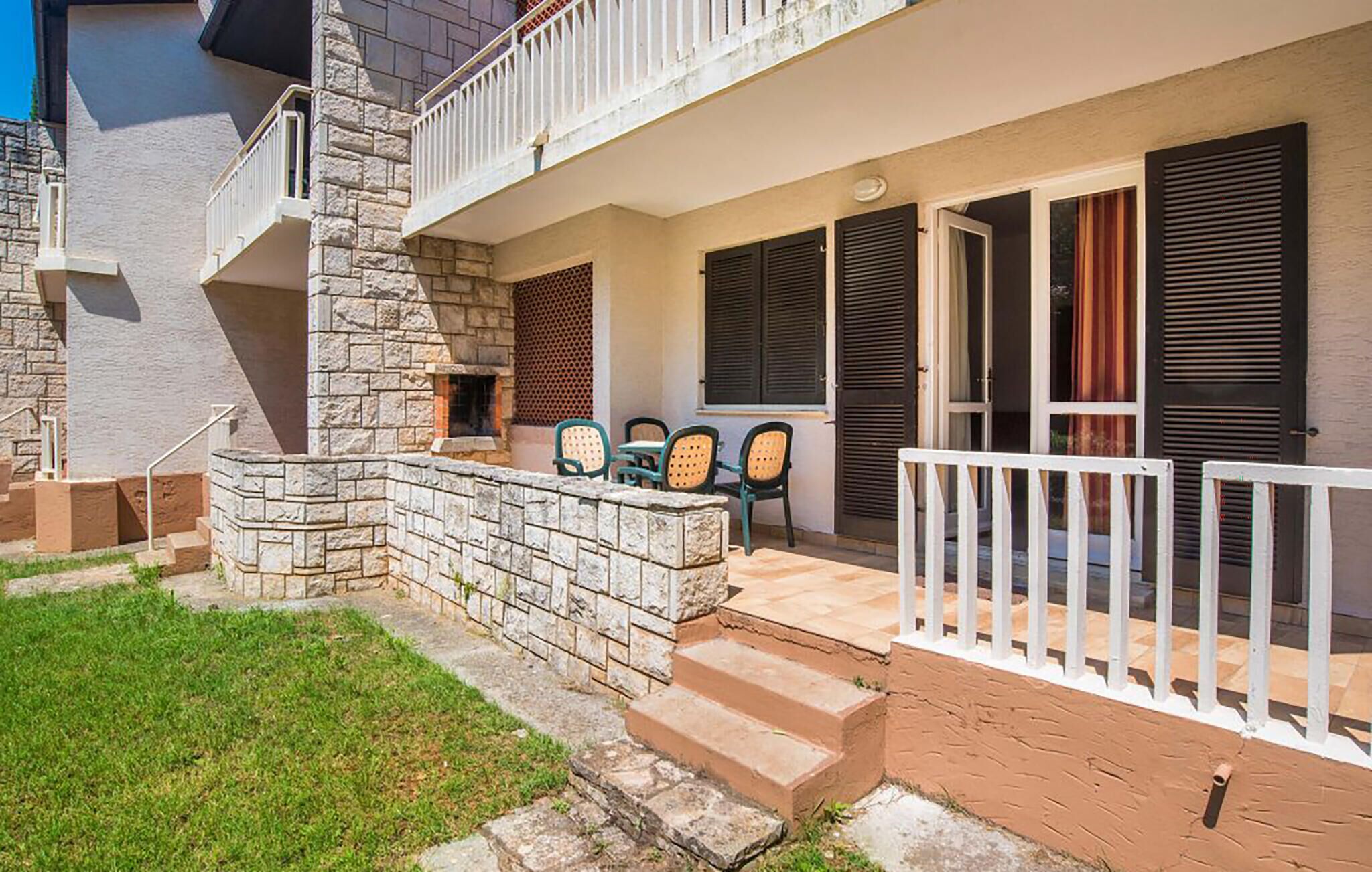 A two-story building with a stone facade, a balcony with chairs, and a small outdoor seating area.