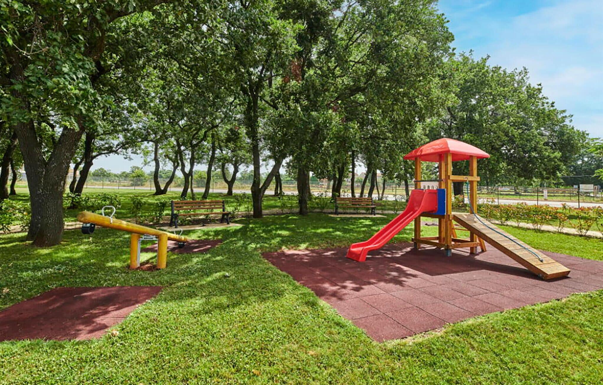 A playground with a slide and swings, surrounded by trees and grass.