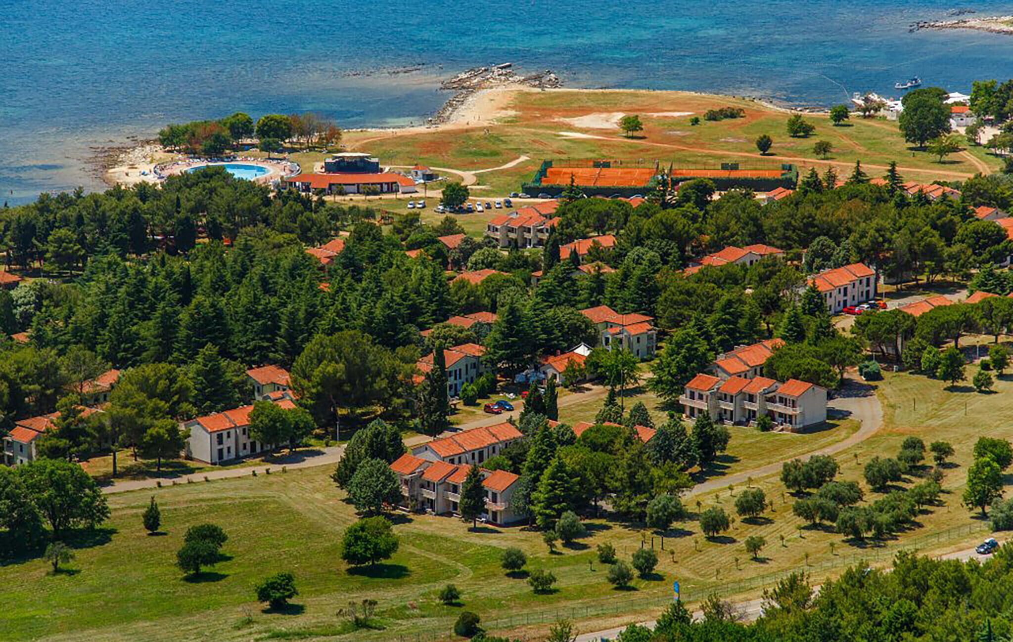 Oversigtsbillede af et kystnære boligområde med huse, en strand og en swimmingpool.