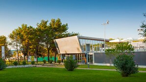 A modern building with a unique sloped roof, surrounded by a well-maintained garden with various plants and trees. - 1 bedroom lovely apartment in Umag (Umag)