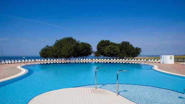 A swimming pool with a wooden deck, surrounded by lounge chairs and trees, with a clear view of the sea. - 1 bedroom lovely apartment in Umag (Umag)