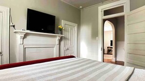 A bedroom with a bed, a TV mounted above a fireplace, and a door leading to another room.