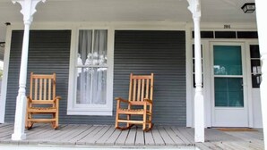 A porch with two wooden rocking chairs, a white door with a glass panel, and a garage door marked "208".
