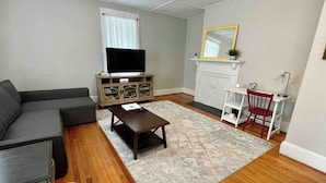 A living room with a grey sofa, a coffee table, a TV on a wooden cabinet, a fireplace, and a red chair.