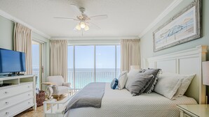 A bedroom with a bed, a television, a chair, a ceiling fan, and a large window with a view. - Boardwalk Beauty: stunning 17th floor condo with private balcony & bunk room (Panama City Beach)