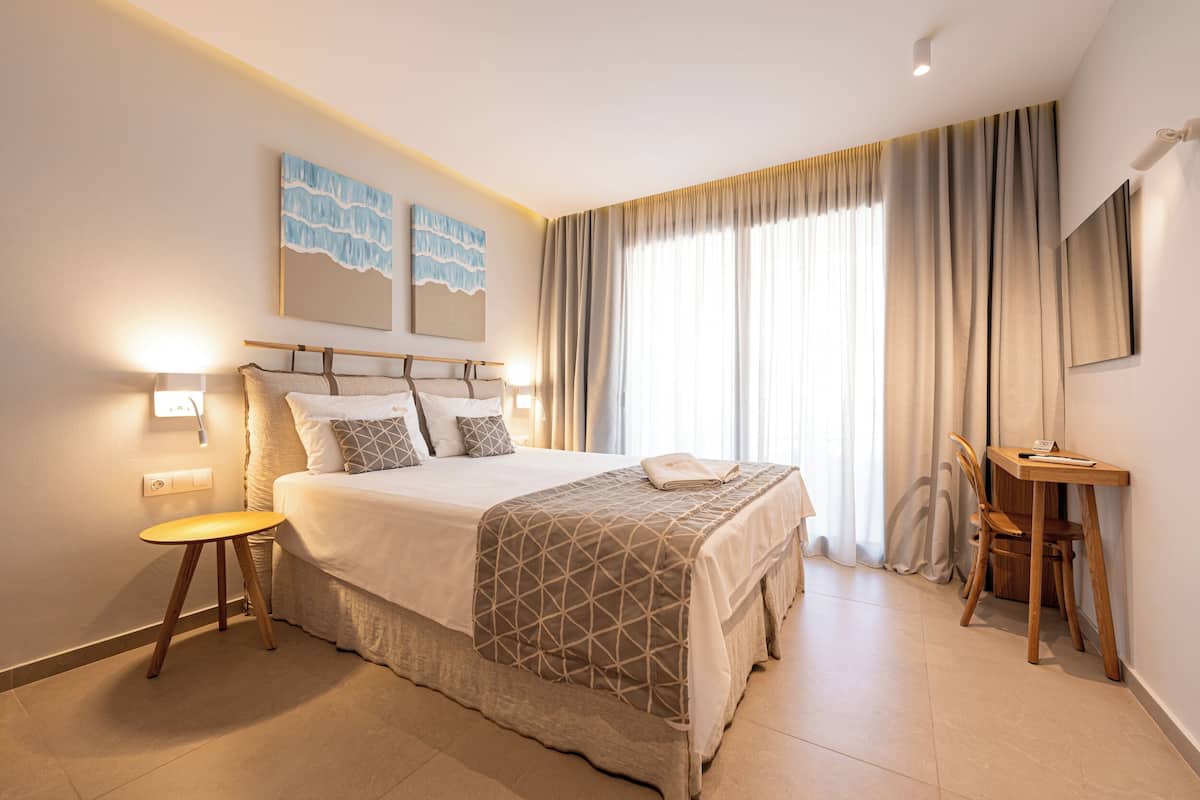 Een hotelkamer met een groot bed, nachtkastje, lamp en een bureau met stoel.