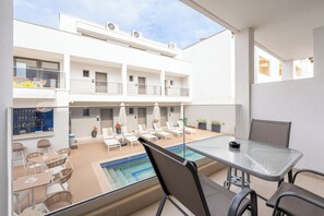Un balcon moderne d’hôtel avec une piscine, des chaises longues et un espace repas.