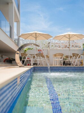 Une piscine à l’eau claire, entourée de chaises et de parasols blancs, et une clôture blanche ornée de motifs décoratifs.