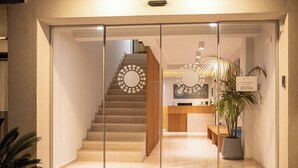 Ein Hotel, dessen Eingang eine Glastür, eine Treppe, ein Empfangstresen und ein Blumentopf zeigen.