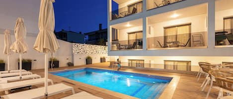 Un edificio de varios pisos con piscina, sillas de descanso y mobiliario exterior.