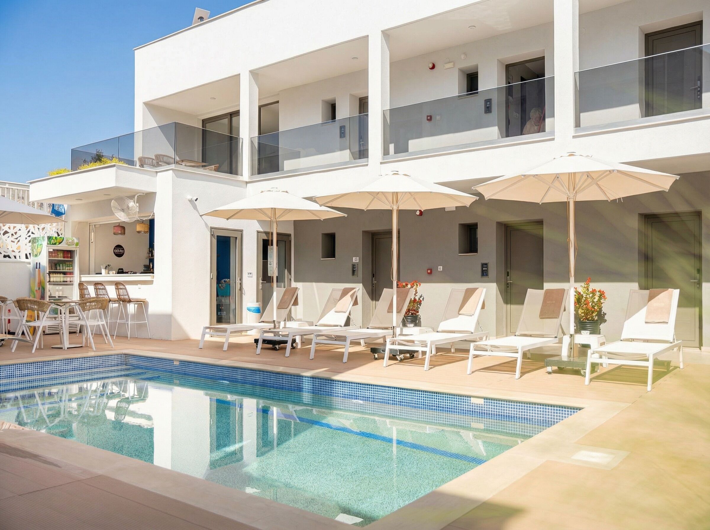 A modern hotel with a pool, sun loungers, and a bar area.