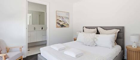 A bedroom with a bed, a chair, a bedside table, and a nightstand.