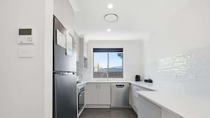 Una cocina moderna con un refrigerador de acero inoxidable, horno empotrado y lavavajillas. Hay una ventana que ofrece vistas al exterior.