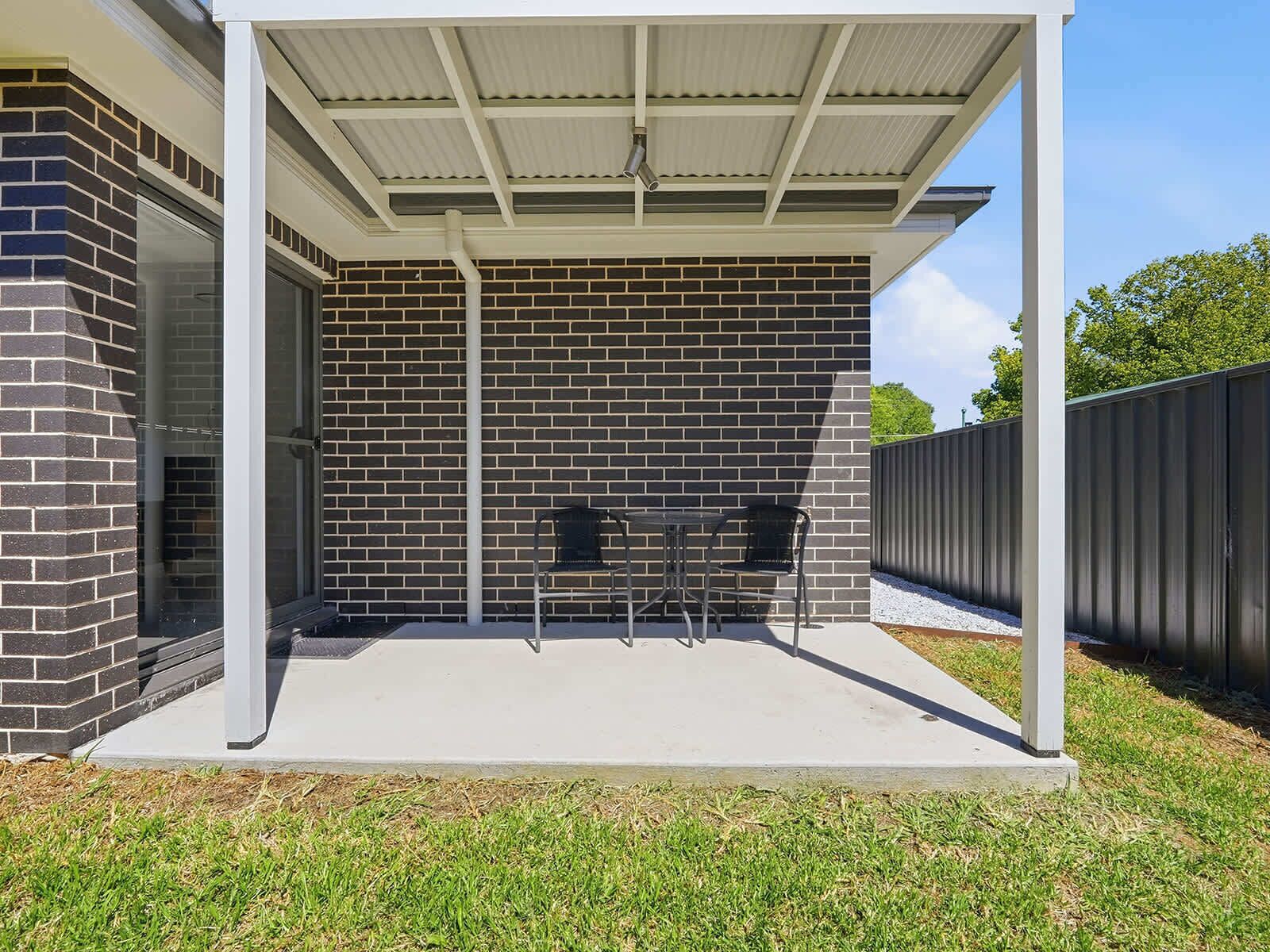 A covered patio area with a brick wall, two chairs, and a concrete floor.