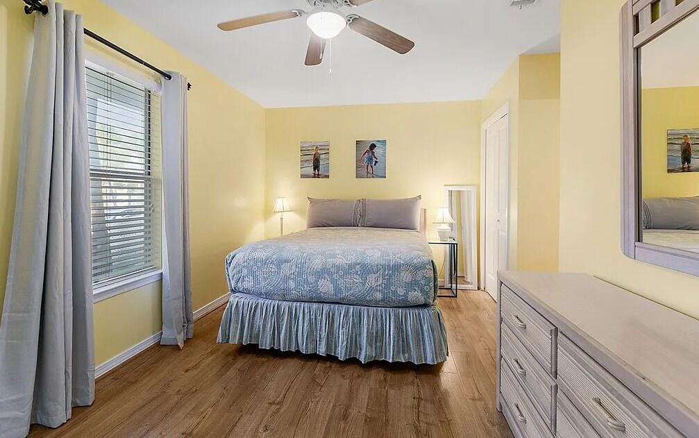 A bedroom with a bed, a ceiling fan, a dresser, and a window with curtains.