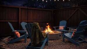 A backyard with a fire pit surrounded by Adirondack chairs, a wooden fence, and string lights. - Upscale Escape • Pool, Hot Tub, Game Room, Firepit (San Antonio)