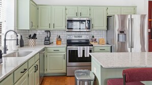 A kitchen with light green cabinets, a stainless steel oven, a microwave, a refrigerator, and a sink. - Upscale Escape • Pool, Hot Tub, Game Room, Firepit (San Antonio)