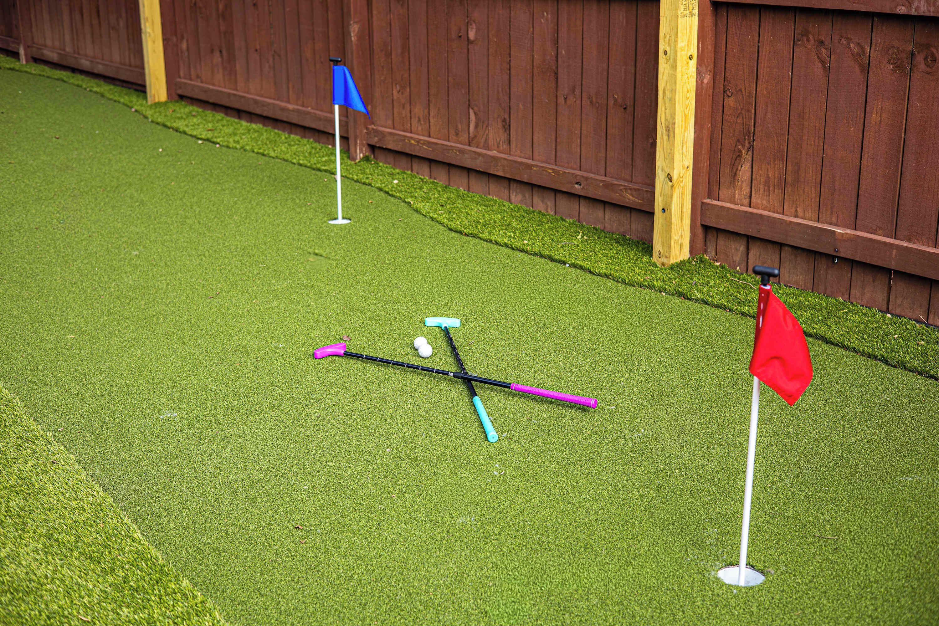 A miniature golf setup with two flags, a golf ball, and two golf clubs on artificial turf.
