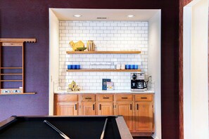 A pool table in a room with wooden cabinets, a white tiled backsplash, and shelves with various items. - Upscale Escape • Pool, Hot Tub, Game Room, Firepit (San Antonio)