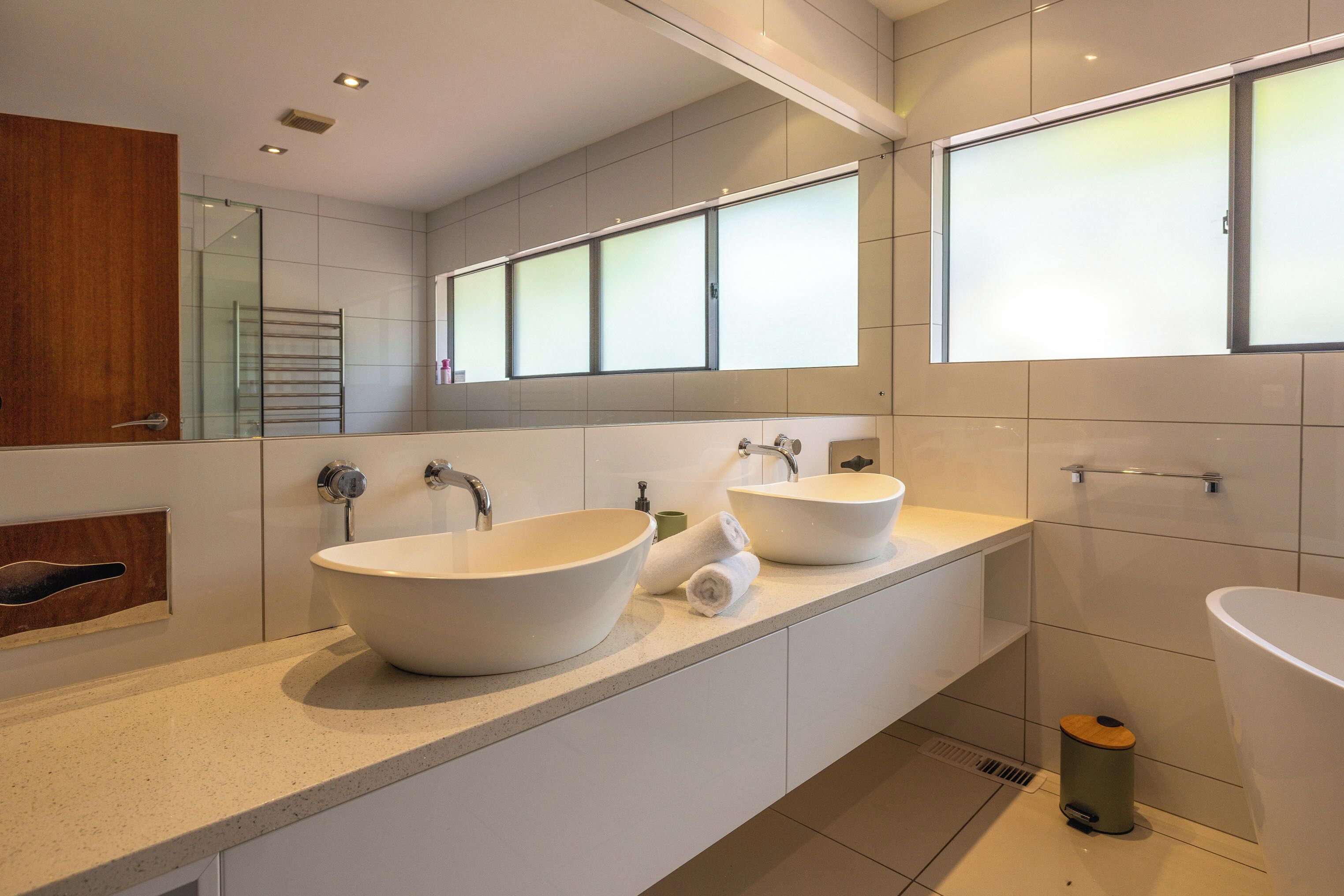 Un baño moderno con dos lavamanos grandes, un espejo y una ventana.