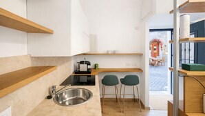 A modern kitchen with wooden shelves, a stainless steel sink, and two green chairs. - Studio Coppelle - Studio Apartment, Sleeps 2 (Rome)