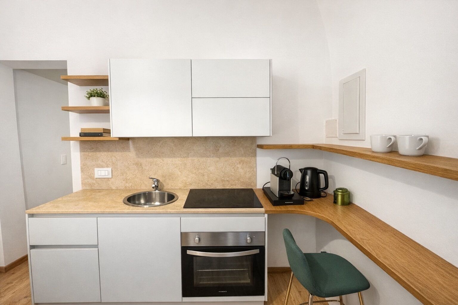 A compact kitchen with a sink, stove, oven, and a small countertop with a kettle and cups.