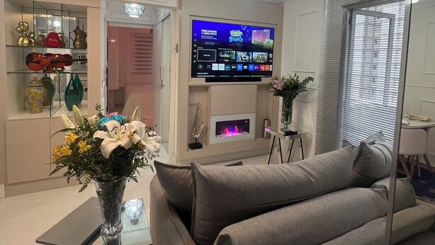 Ein modernes Wohnzimmer mit Flachbildfernseher, Glastisch und grauem Sofa.