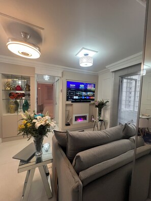 A modern living room with a flat-screen TV, a glass coffee table, and a grey sofa. - Apto familiar fabuloso em condomínio/Interlagos, Zona Sul/IBC (Campo Grande)