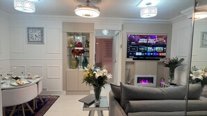 Ein modernes Wohnzimmer mit Flachbildfernseher, einem Essbereich mit rundem Tisch und Stühlen sowie einer Couch.