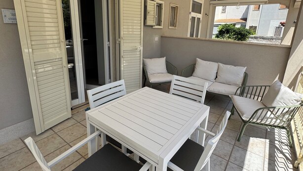En terrasse med et hvidt bord og stole, en sofa og et vindue med udsigt til en bygning.