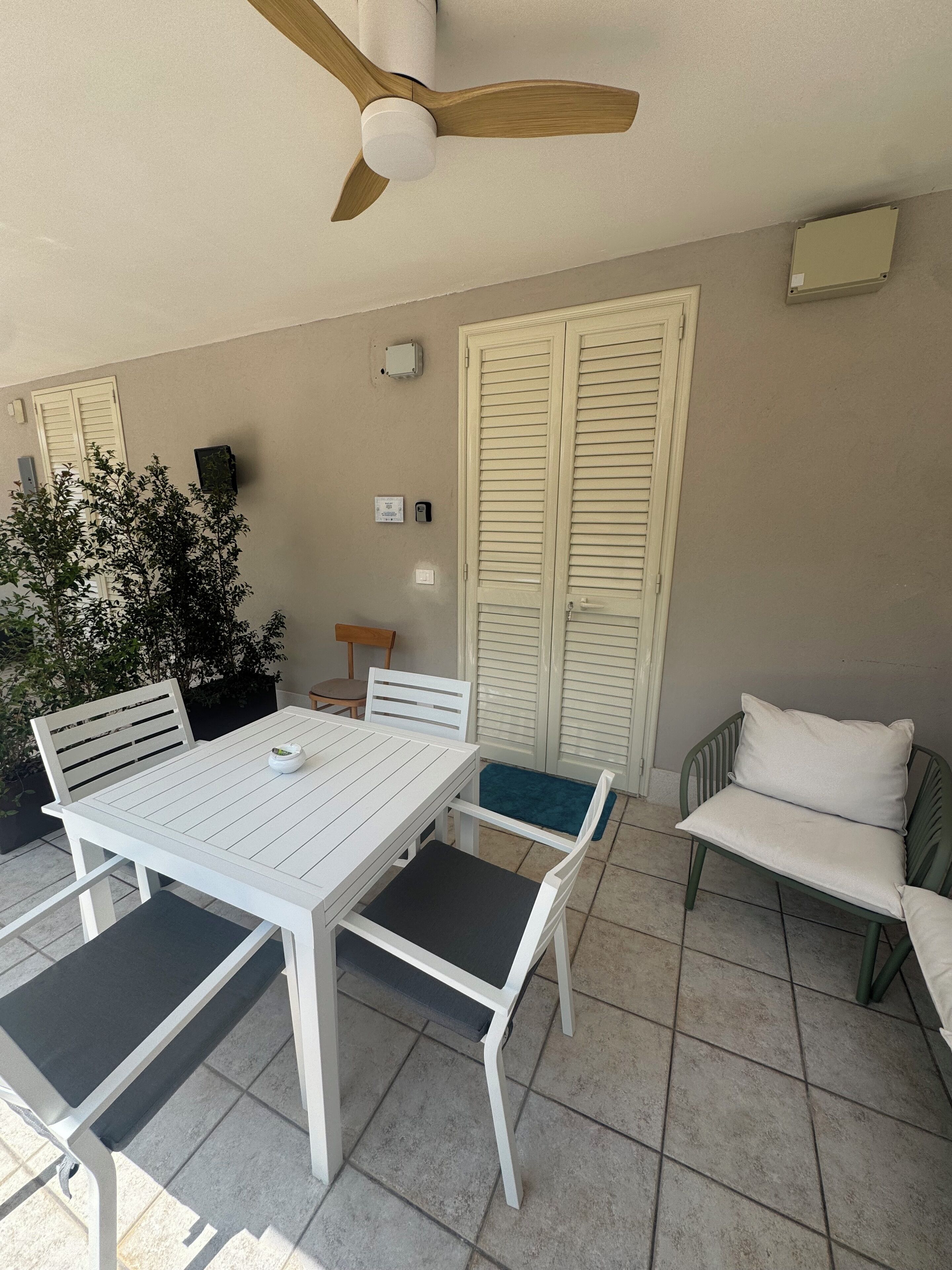 A patio with a white table and chairs, a ceiling fan, a potted plant, and a sliding door.