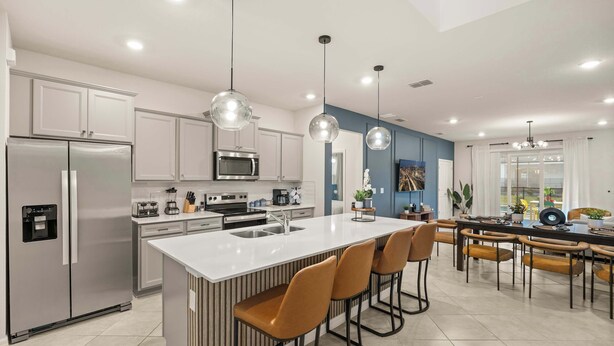 Une cuisine moderne dotée d’un îlot central, d’appareils électroménagers en acier inoxydable et de luminaires suspendus.