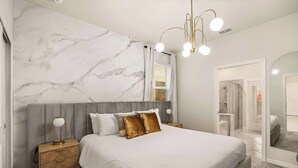 Une chambre à coucher avec une tête de lit en marbre, un lit avec une literie blanche, une table de chevet avec une lampe et un miroir.
