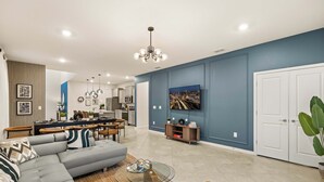 Un salon moderne avec un canapé d’angle, une table basse en verre et un coin repas, la cuisine étant visible au fond.