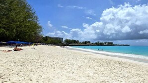 Een strand met helder turquoise water, een zandstrand en enkele parasols.
