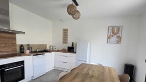 A modern kitchen with white cabinets, a wooden dining table, and a hanging light fixture. - House Rochemaure (Rochemaure)