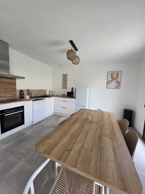 A modern kitchen with white cabinets, a wooden dining table, and a hanging light fixture. - House Rochemaure (Rochemaure)