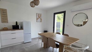 A modern kitchen with white cabinets, a white refrigerator, and a wooden dining table with four chairs. There is a window with a view of greenery outside. - House Rochemaure (Rochemaure)