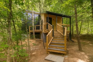 Eine Holztreppe führt zu einer kleinen Hütte in bewaldetem Gelände.