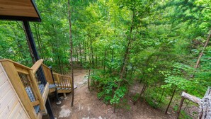 Eine Holzterrasse mit einer Treppe, die zu einem überdachten Bereich führt, umgeben von dichtem Wald.