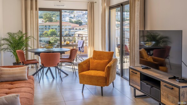 A modern living room with a sofa, armchairs, a dining table, and a TV.