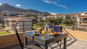 Un balcón con una mesa lista para el desayuno, con vistas a una zona residencial que incluye edificios y una montaña al fondo.