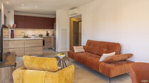 Un salon moderne avec un canapé, deux fauteuils, une table basse et une cuisine en arrière-plan.